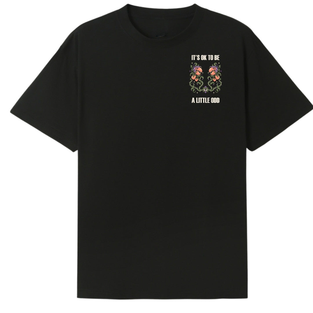 A black oversized tee with a small It's OK To Be A Little Odd graphic on the left chest.