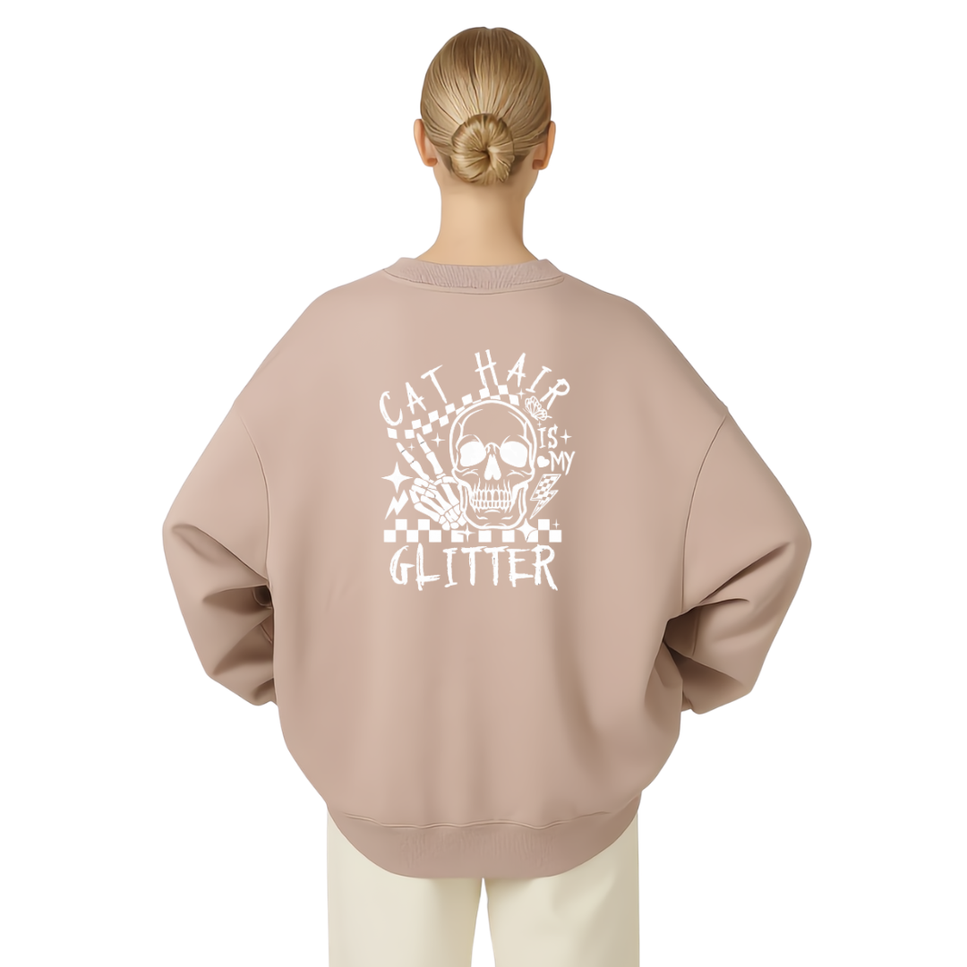 A woman viewed from the back wearing an oversized crewneck sweatshirt in a dusty rose pink color with a white graphic print on the back featuring a skull, cat hair, and the words 'CAT HAIR GLITTER'.