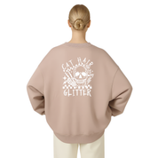 A woman viewed from the back wearing an oversized crewneck sweatshirt in a dusty rose pink color with a white graphic print on the back featuring a skull, cat hair, and the words 'CAT HAIR GLITTER'.