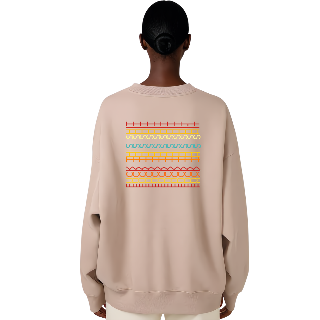 A person shown from the back wearing a light beige crewneck sweatshirt with a colorful geometric pattern printed across the upper back. The pattern features horizontal stripes in red, yellow, and light blue.