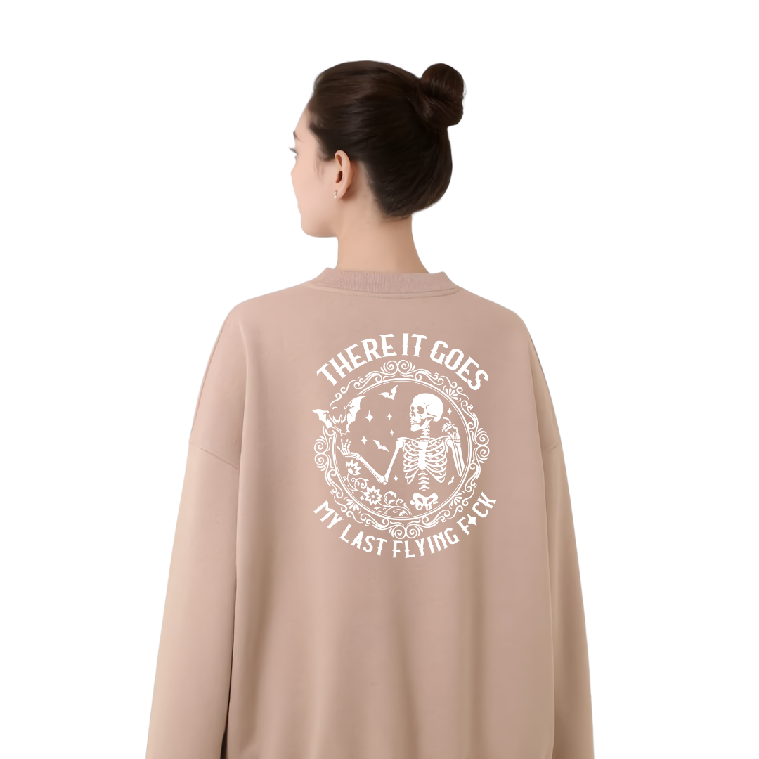 A woman shown from the back wearing a beige crewneck sweatshirt with a large white graphic print on the back featuring a skeleton and the text 'THERE IT GOES MY LAST FLYING FACK'.