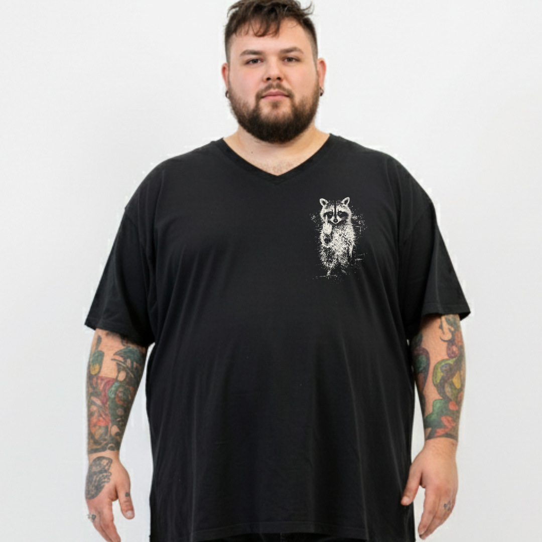 A man with a beard and tattooed arms wearing a black v-neck t-shirt with a white raccoon graphic on the left chest, photographed against a light gray background.