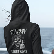 Person wearing a black hoodie with a skull graphic and text by the ocean