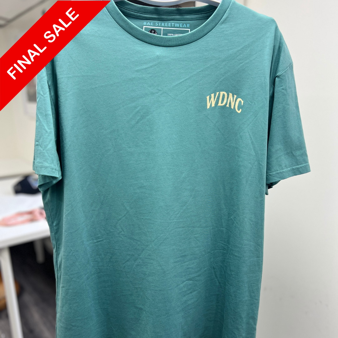 Green t-shirt with 'WDNC' logo on a hanger against a neutral background