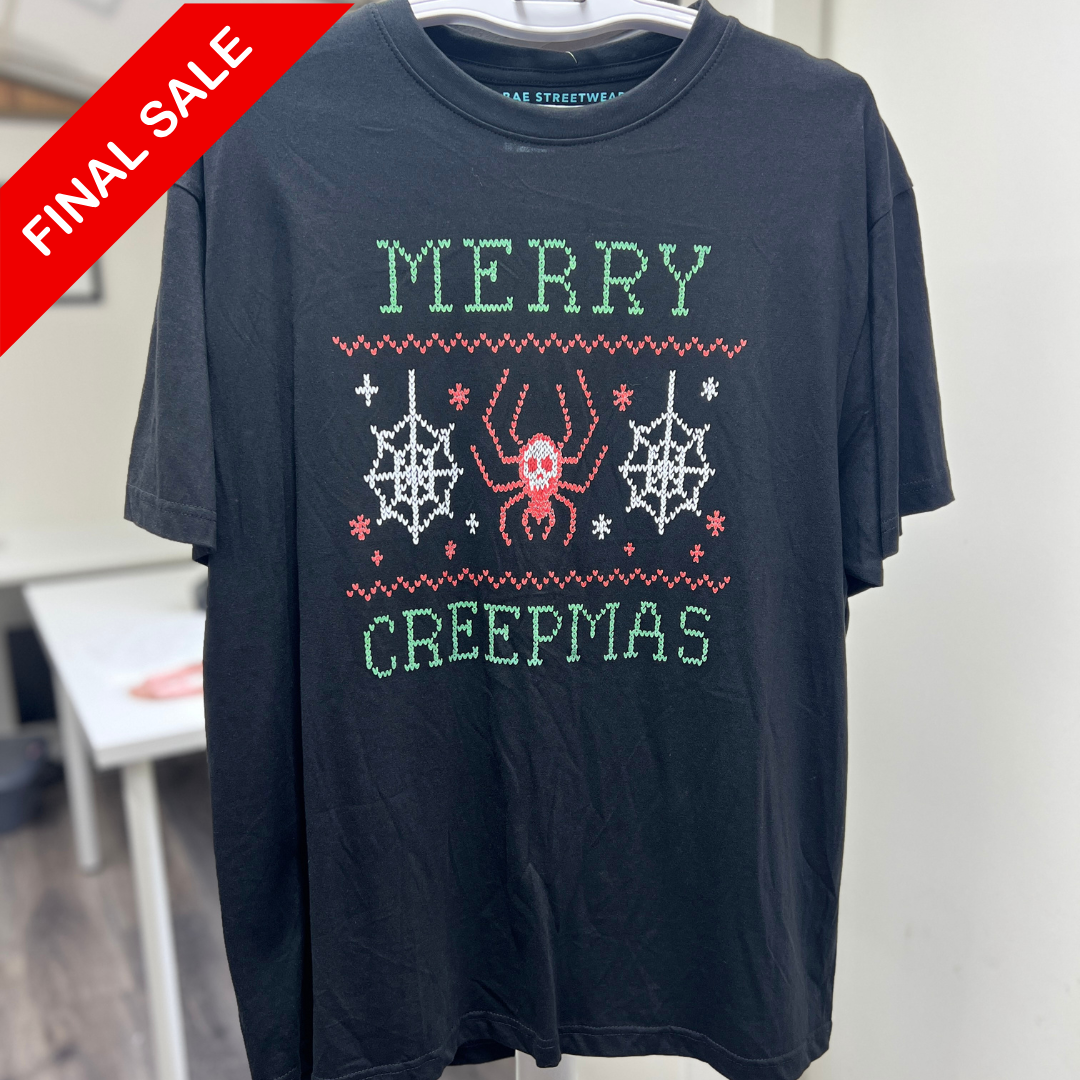 Black t-shirt with 'Merry Creepmas' design featuring a spider and webs, on a hanger.