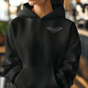 Black hoodie with a bat emblem worn by a person, blurred background