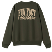 An olive green crewneck sweatshirt shown from the back, featuring a distressed beige graphic print that reads 'FUN FACT i don't care' with a small flag design above it.