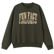 An oversized crewneck sweatshirt in dark olive green with a distressed beige graphic on the chest that reads 'FUN FACT I don't care' with a checkerboard pattern.