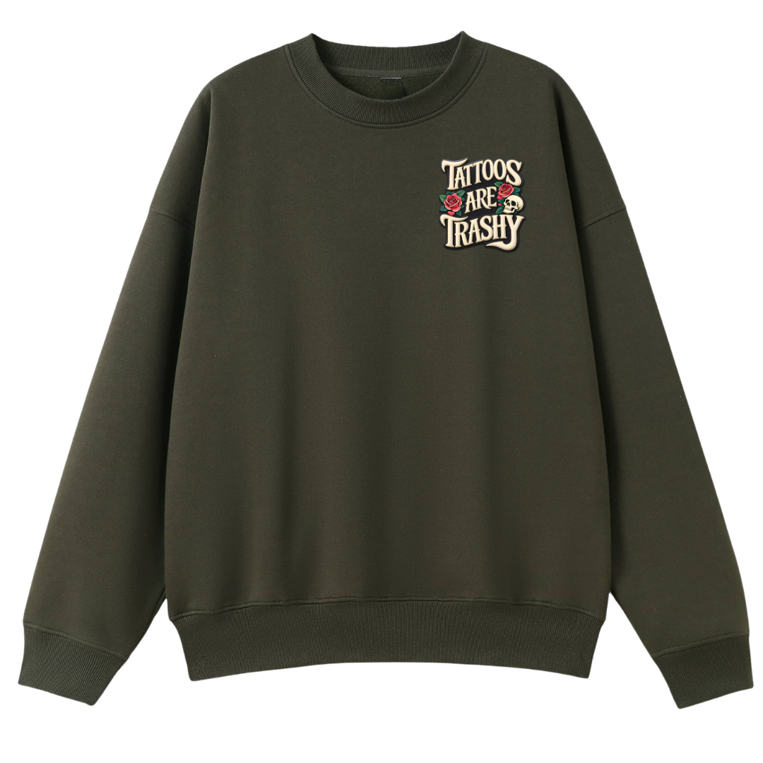 An olive green crewneck sweatshirt with a graphic on the left chest that reads 'TATTOOS ARE TRASHY' in cream lettering, accented with small red and white skulls and roses, shown against a plain white background.
