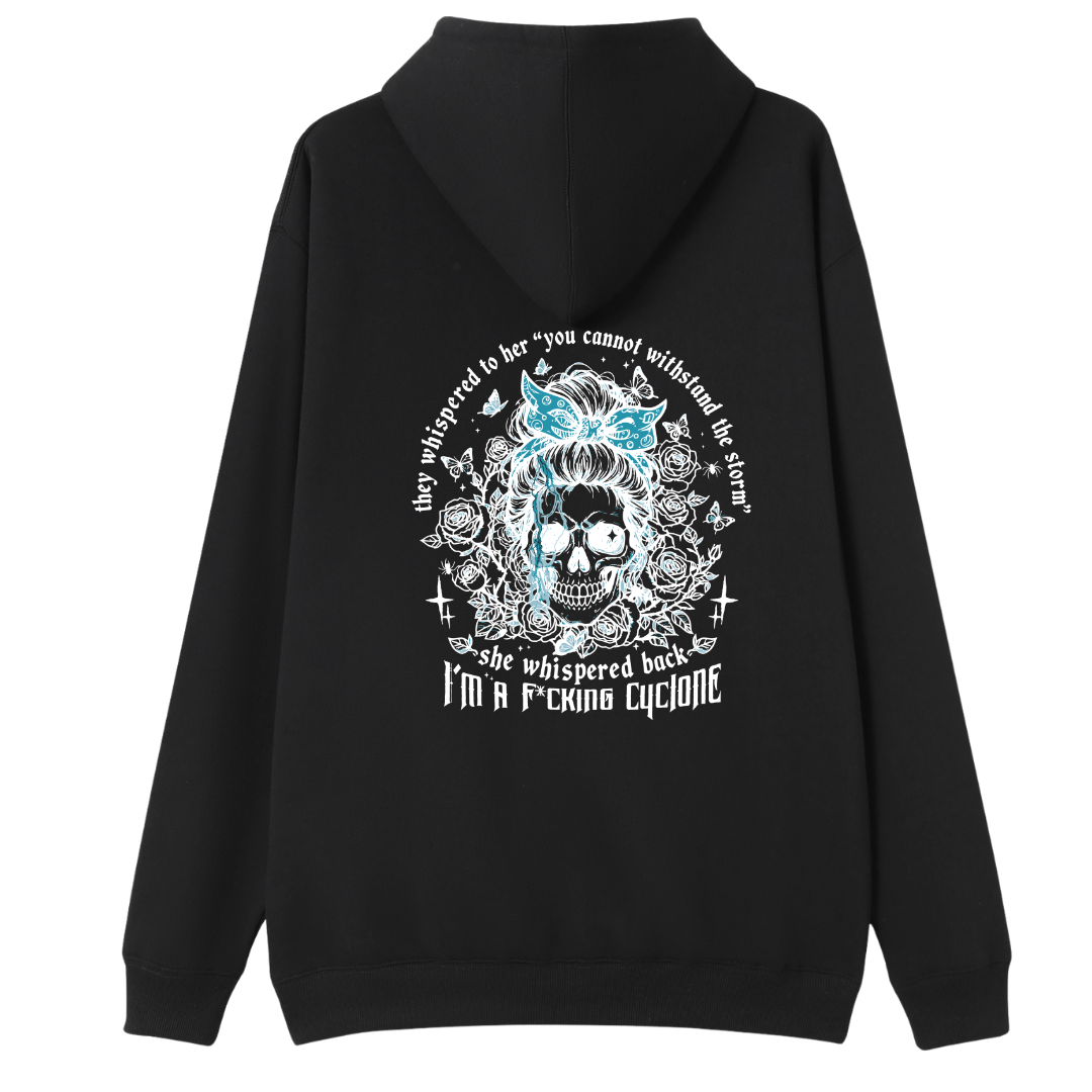 A black pullover hoodie shown from the back, featuring a large graphic print of a skull with a blue bow and white text that reads 'They whispered to her "you cannot withstand the truth, she whispered back I'm a f*cking cyclone"'.