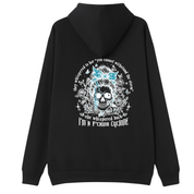A black pullover hoodie shown from the back, featuring a large graphic print of a skull with a blue bow and white text that reads 'They whispered to her "you cannot withstand the truth, she whispered back I'm a f*cking cyclone"'.