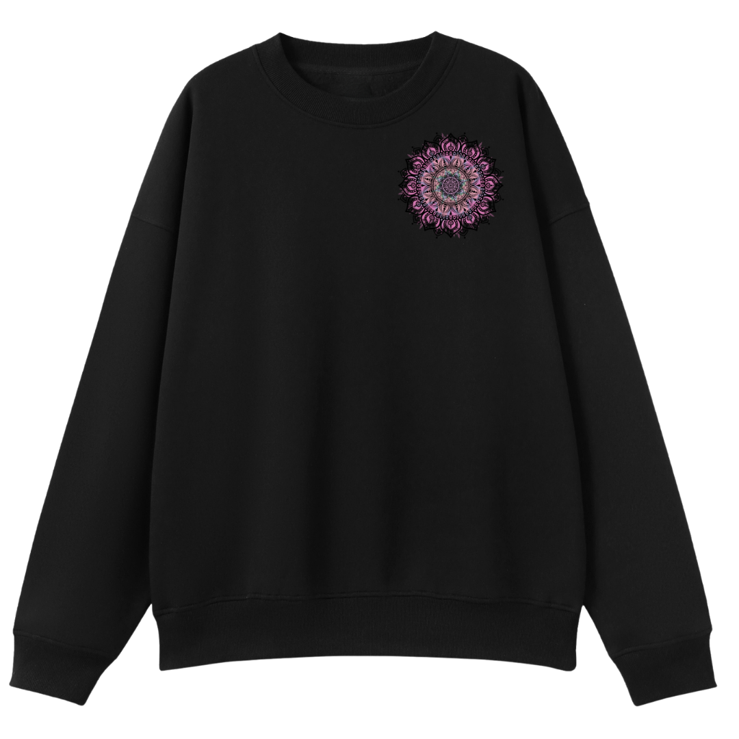 A black crewneck sweatshirt with a small circular mandala graphic on the left chest in shades of purple, pink, and white, displayed against a solid white background.