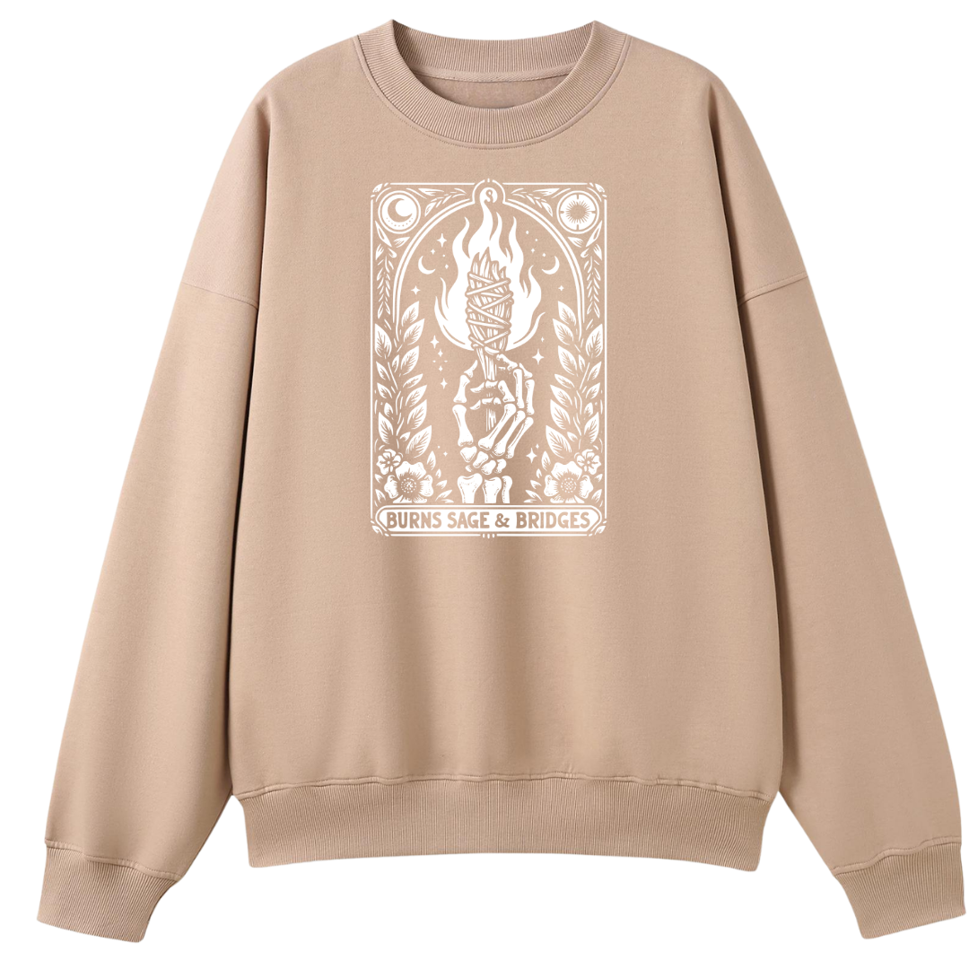 A beige crewneck sweatshirt featuring a white graphic print on the front with a hand holding a flaming torch and the text 'BURNS SAGE & BRIDGES'.