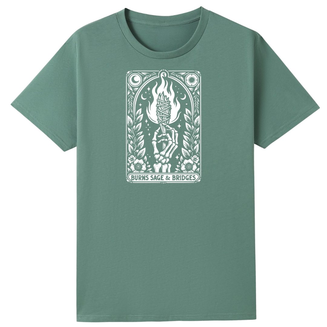 A sage green short-sleeve crewneck t-shirt featuring a white tarot card graphic on the chest. The graphic depicts a burning candle held by a skeletal hand, with the text 'BURNS SAGE & BRIDGES' printed below.