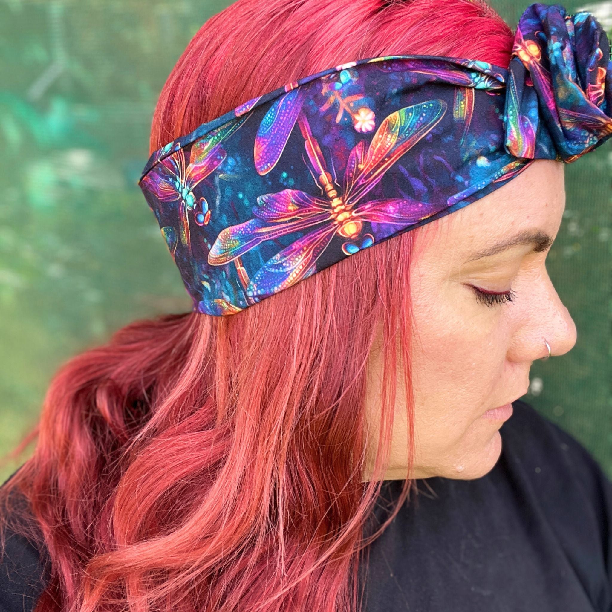 wearing a wire headwrap adorned with a kaleidoscope of colors, the pattern dragonflys. The headwrap is tied stylishly off to the side