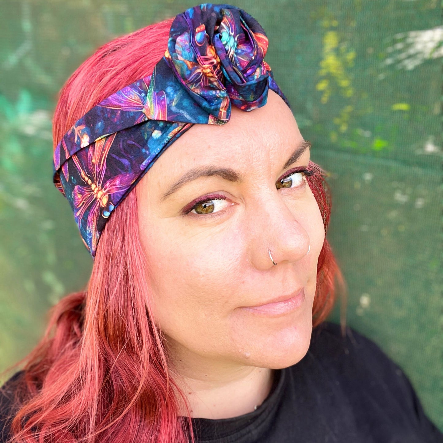 wearing a wire headwrap adorned with a kaleidoscope of colors, the pattern dragonflys. The headwrap is tied stylishly off to the side