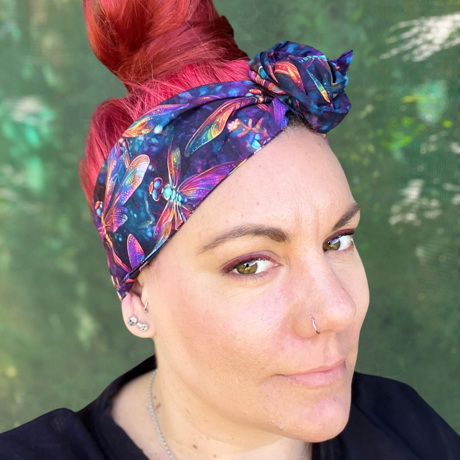 wearing a wire headwrap adorned with a kaleidoscope of colors, the pattern dragonflys. The headwrap is tied stylishly off to the side