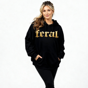 Woman wearing a black hoodie with 'feral' in gold letters on a white background