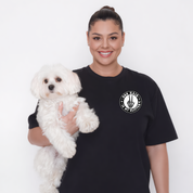 Woman holding a white dog wearing a black t-shirt with a logo on a white background