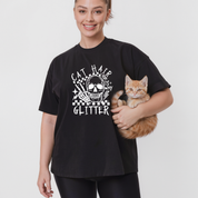 Person wearing a black t-shirt with a cat graphic and text, holding a cat.