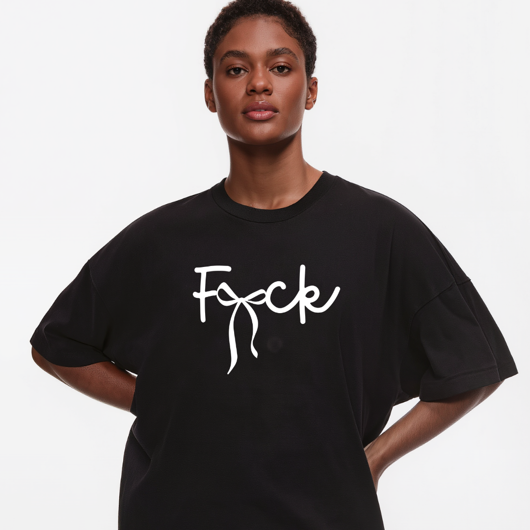 A model wearing an oversized black t-shirt with the word 'Fuck' printed in white script across the chest, set against a plain light gray background.