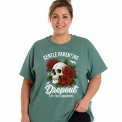 A woman wearing a sage green graphic t-shirt with a skull and red roses design, featuring the text 'GENTLE PARENTING Dropout EST: THIS MORNING'.