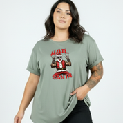 Woman wearing a green t-shirt with a graphic design of a person in a Santa Claus outfit and text 'HAIL SANTA' on a plain background.