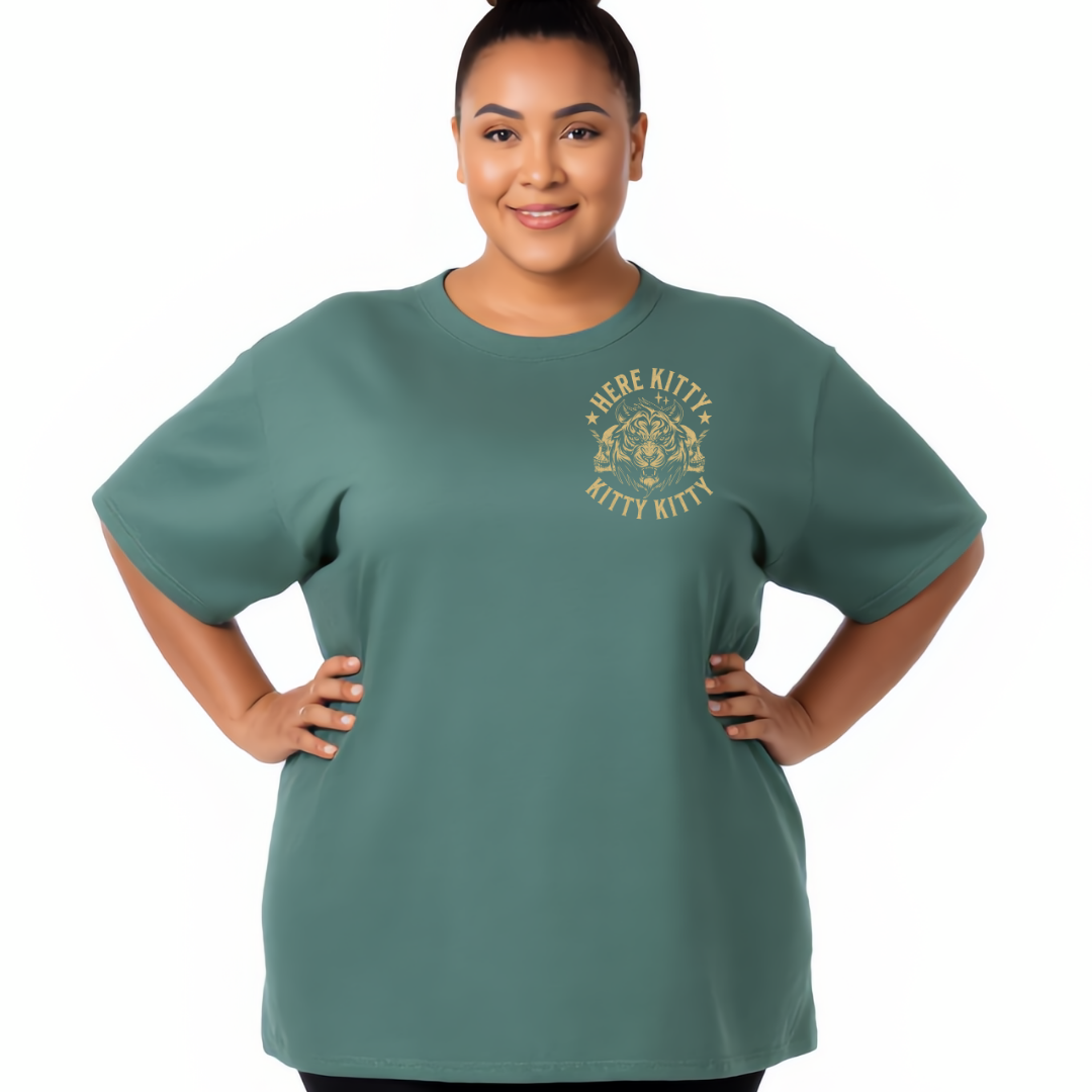 A woman modeling a muted teal green short-sleeve t-shirt with a gold 'HERE KITTY KITTY KITTY' graphic on the left chest, set against a plain white background.