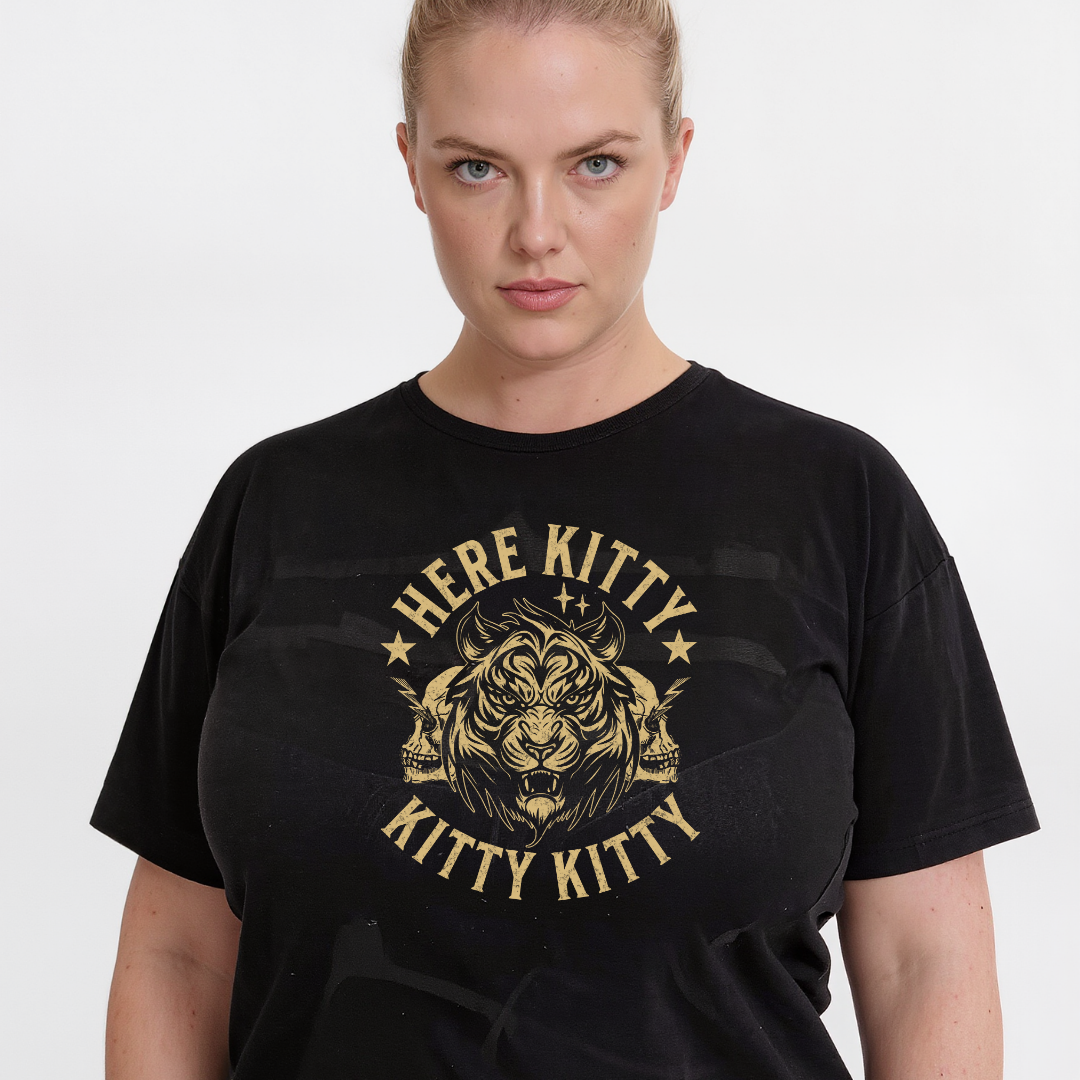 A woman wearing a black short-sleeve graphic t-shirt with a distressed gold design featuring a tiger head and the text 'HERE KITTY KITTY'.