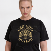 A woman wearing a black short-sleeve graphic t-shirt with a distressed gold design featuring a tiger head and the text 'HERE KITTY KITTY'.