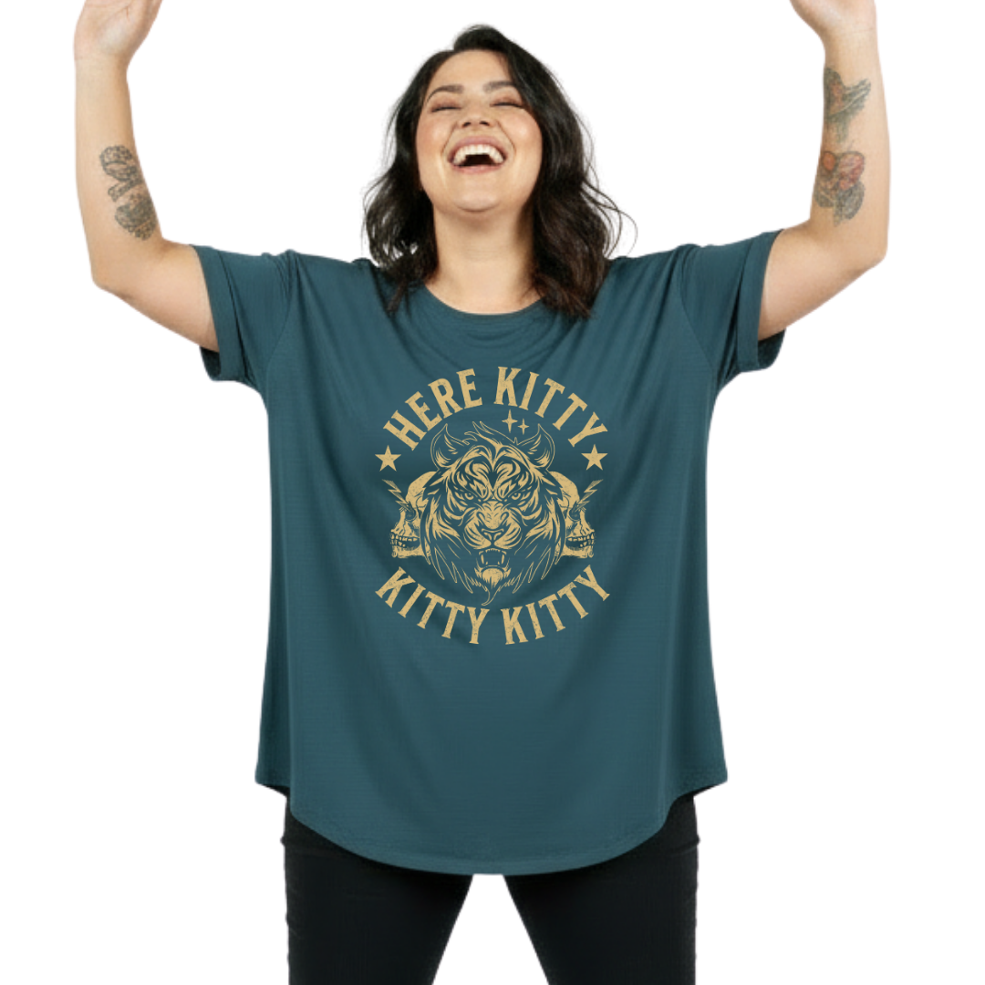 A woman with raised arms is wearing an oversized teal t-shirt featuring a gold graphic of a lion and the text 'HERE KITTY KITTY KITTY'.