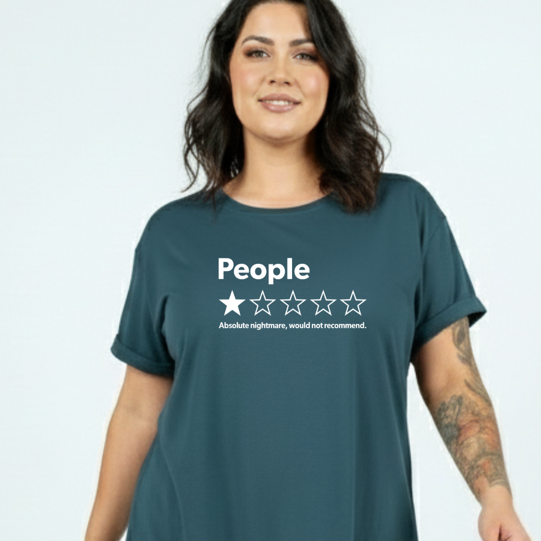 A woman wearing a dark teal graphic t-shirt with a white rating design that reads 'People' and 'Absolute nightmare, would not recommend.' against a light gray background.