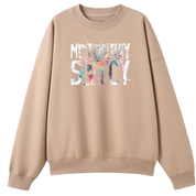 A beige crewneck sweatshirt with a colorful graphic text print reading 'MERRY SATCY' on the chest, displayed against a solid white background.