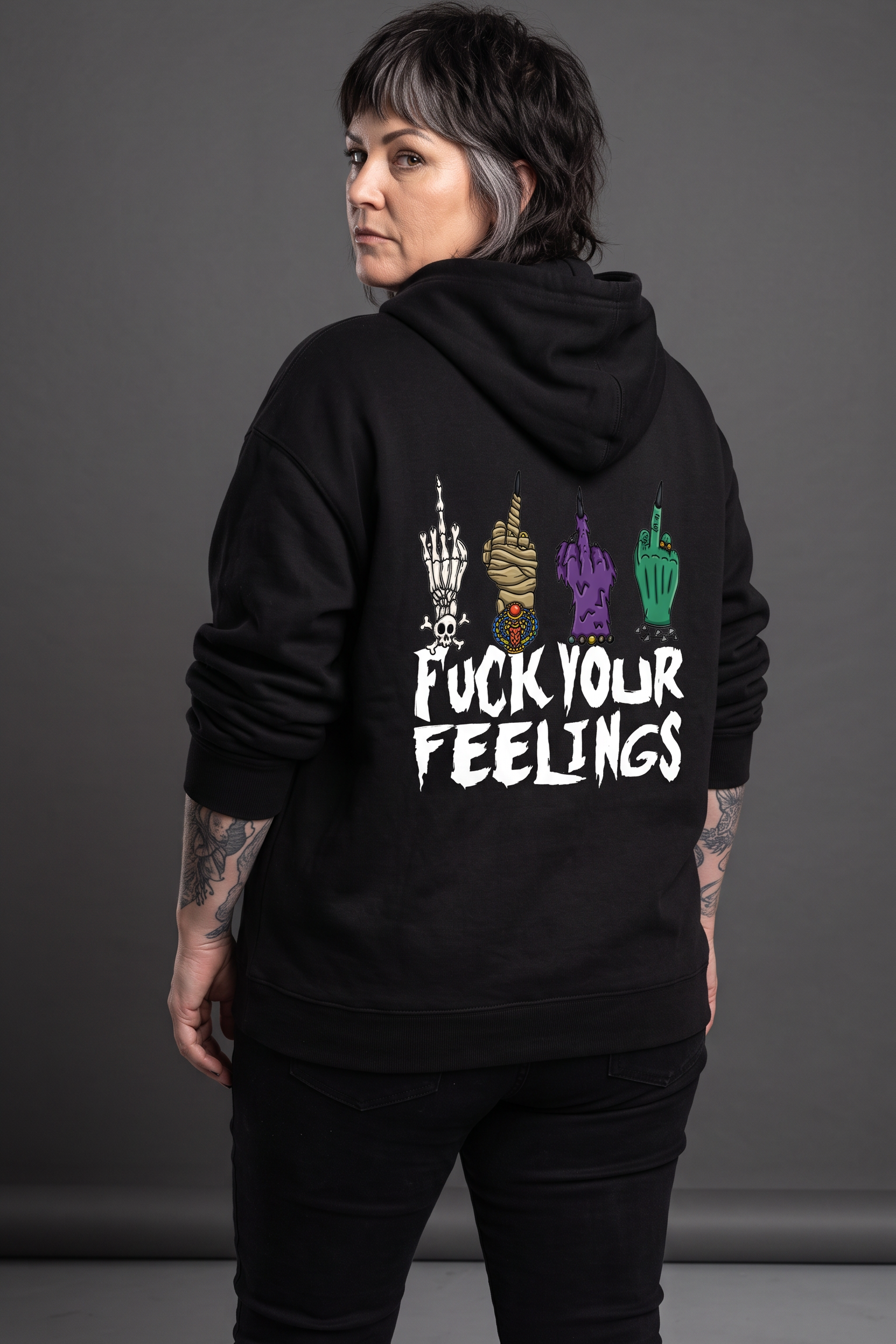 A person shown from the back wearing a black hoodie with a graphic print on the back. The print features four colorful hand gestures in white, purple, green, and red, above the text 'FUCK YOUR FEELINGS' in white.