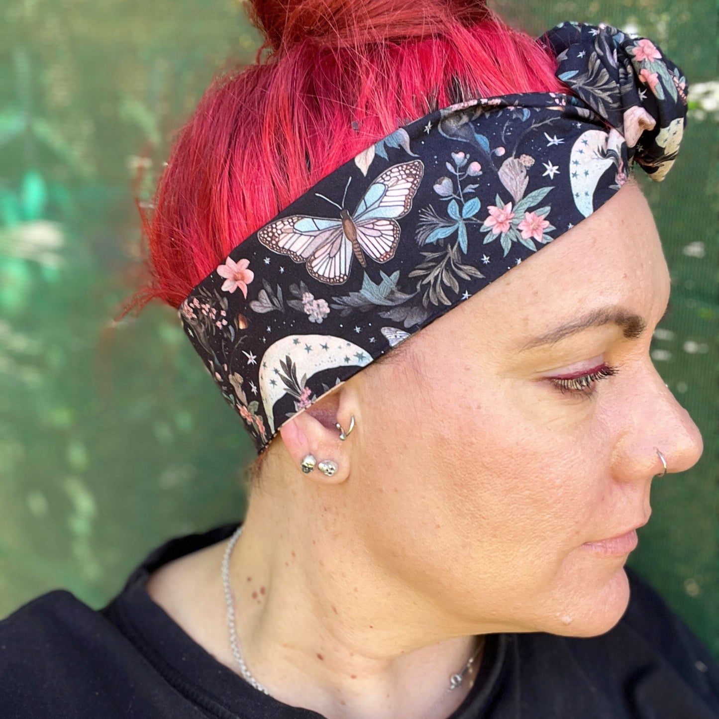  a wire headwrap featuring a mystical garden theme. The headwrap is black and illustrated with delicate butterflies, stars, and an array of soft-colored flowers, creating an enchanting look. It is tied at the top, adding an elegant twist to the design