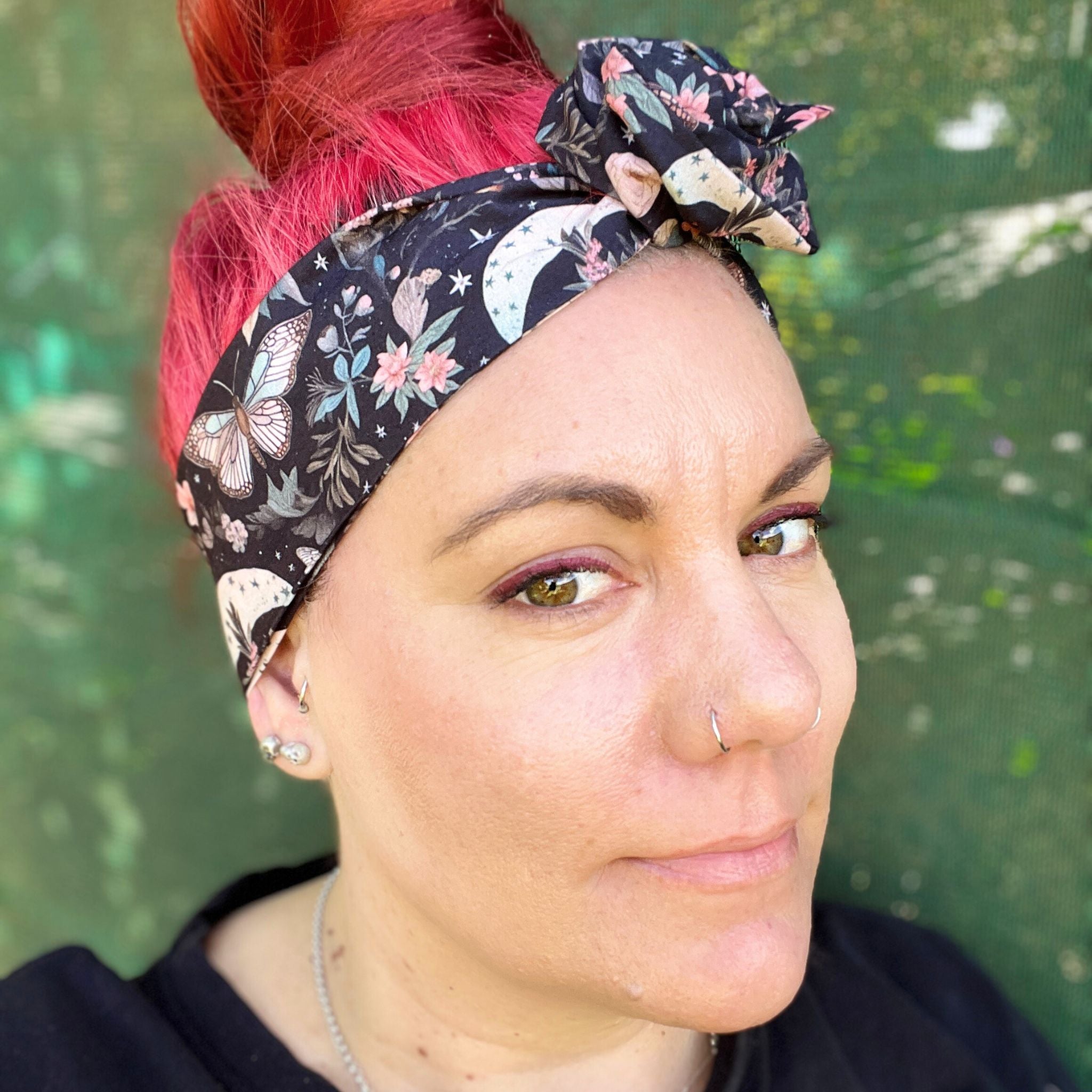  a wire headwrap featuring a mystical garden theme. The headwrap is black and illustrated with delicate butterflies, stars, and an array of soft-colored flowers, creating an enchanting look. It is tied at the top, adding an elegant twist to the design