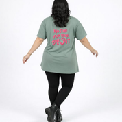 Person wearing a green t-shirt with pink text on the back, standing against a white background
