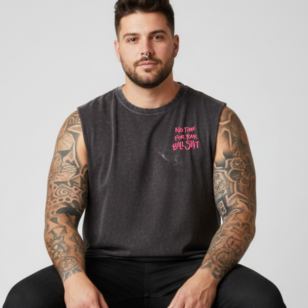 Man wearing a sleeveless black shirt with pink text, sitting against a plain background