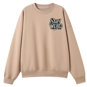 A beige crewneck sweatshirt with a black and white graphic text print reading 'Stay WEIRD' on the left chest, displayed on a solid white background.