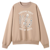 A beige crewneck sweatshirt with a white graphic print of a skeleton in a coffin and the text 'SURVIVING PURELY OUT OF SPITE' on the front, displayed against a solid white background.