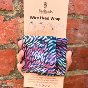 Wire head wrap with colorful pattern held against a brick wall, featuring Bae Bands packaging.