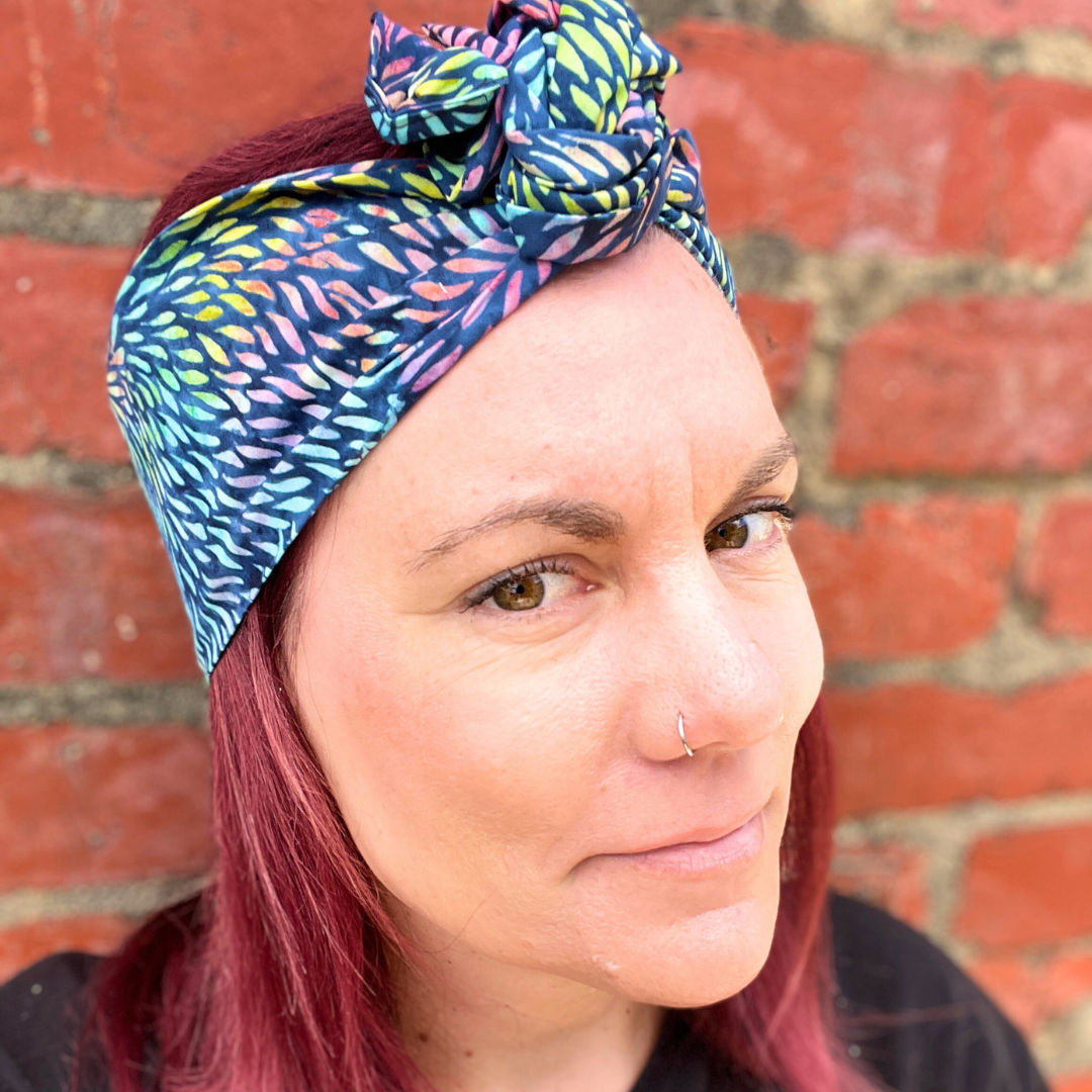 Woman wearing a colorful headscarf against a brick wall.