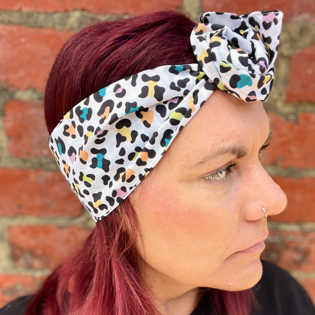 Woman wearing a colorful leopard print headband against a brick wall.