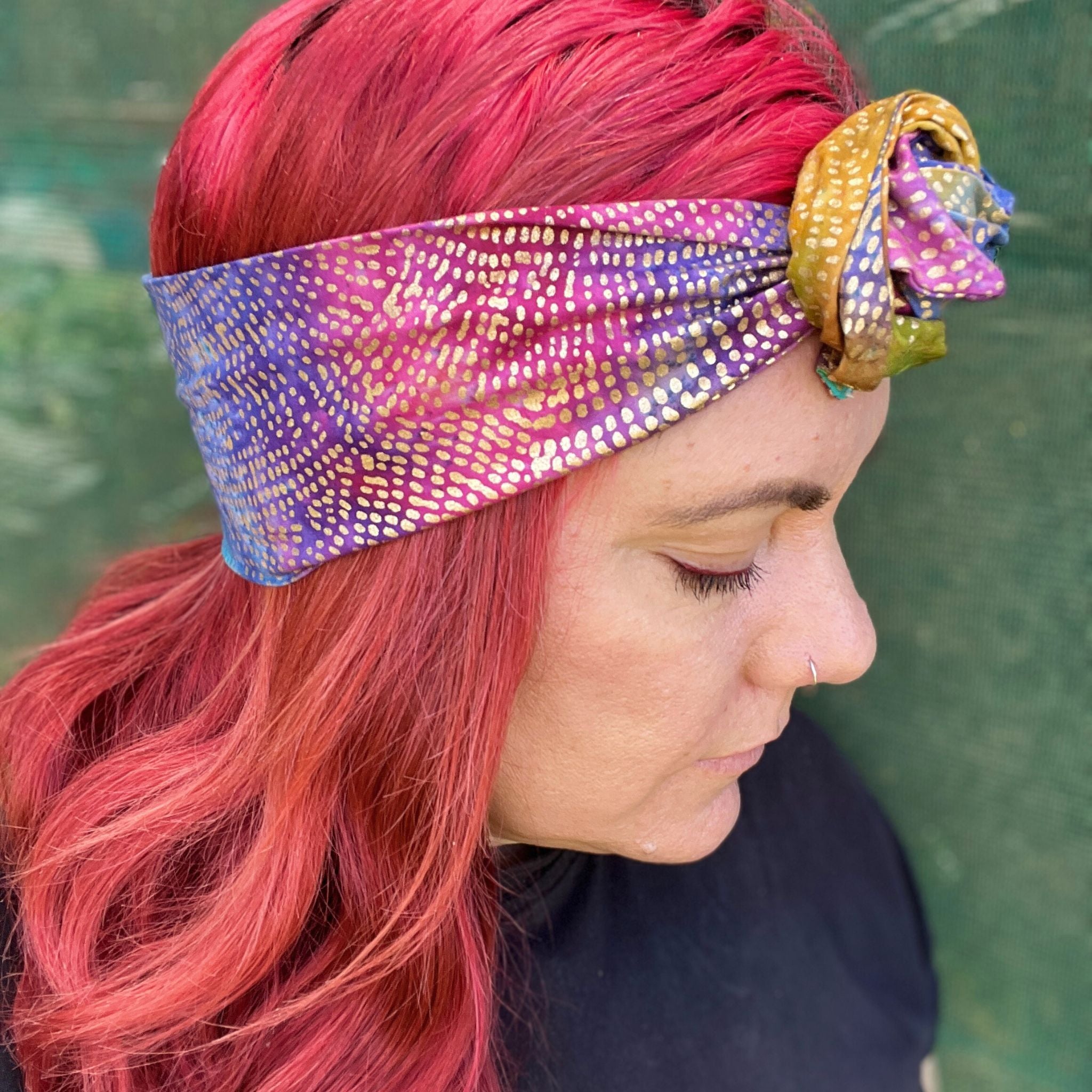 wire headwrap featuring a radiant metallic sheen with a gradient of colors, resembling a rainbow effect. The headwrap is artfully tied in a knot at the side of her head, lending a touch of whimsy to the overall look. 
