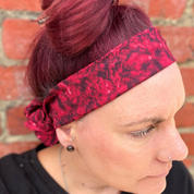 Person wearing a red patterned headband against a brick wall.