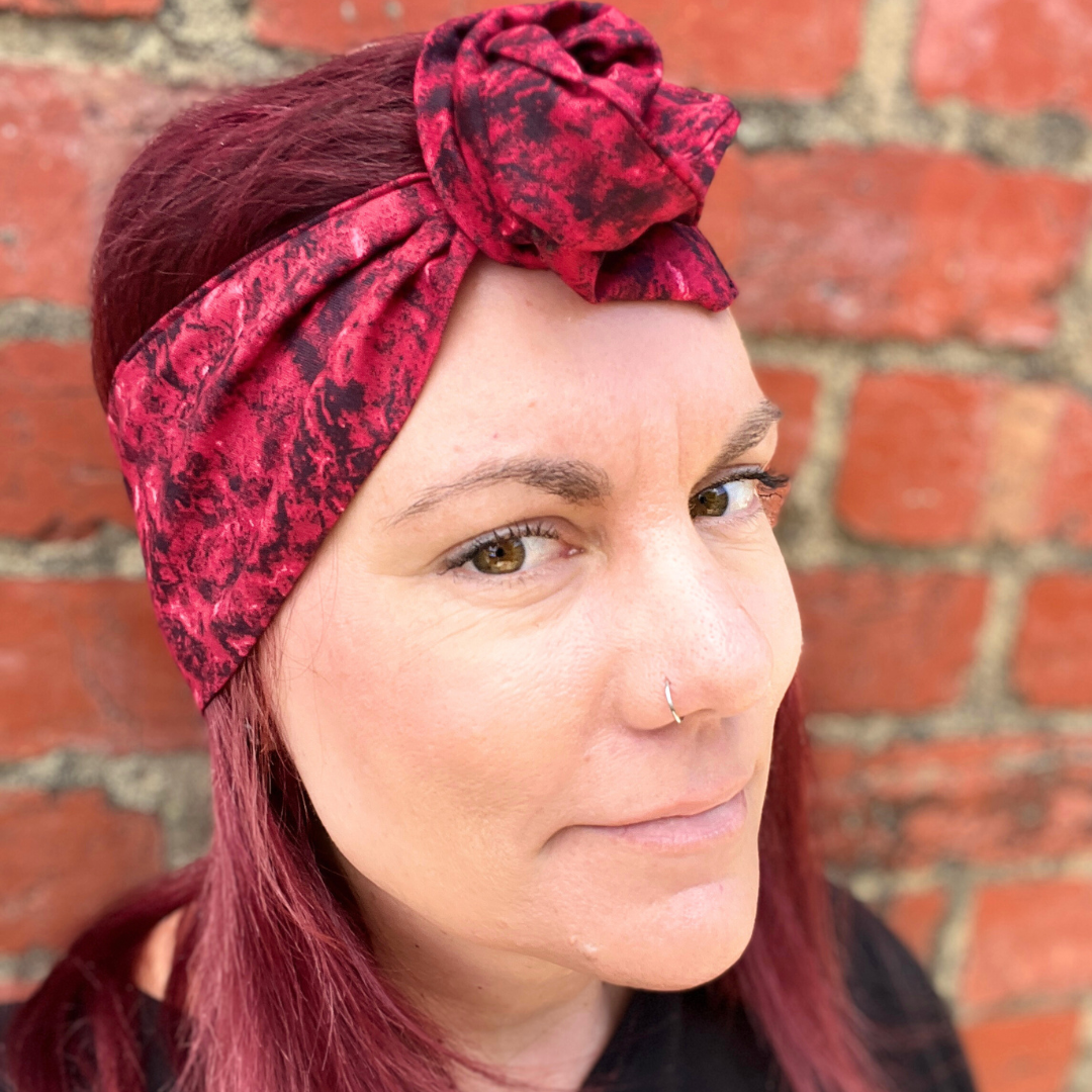 Woman wearing a red patterned headscarf against a brick wall