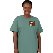 A woman wearing a sage green short-sleeve t-shirt with a graphic of a white skull surrounded by red roses on the left chest, set against a plain white background.