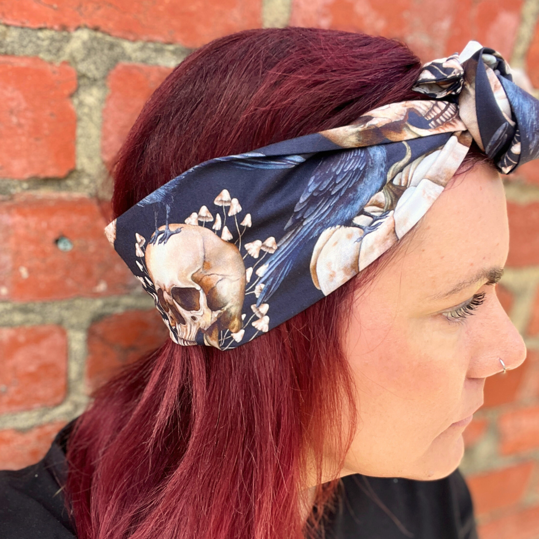 Person wearing a skull and floral patterned headband against a brick wall.