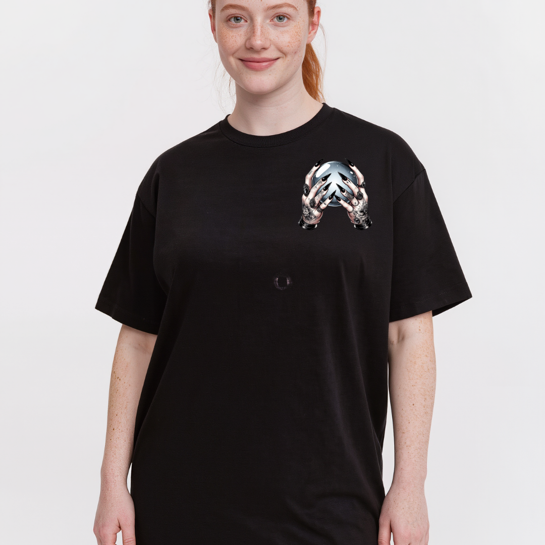 A woman wearing a black oversized short-sleeve t-shirt with a metallic silver and black graphic print on the left chest, set against a plain light gray background.