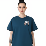 A woman modeling an oversized dark teal t-shirt with a small graphic print of a stylized skull on the left chest, set against a plain white background.